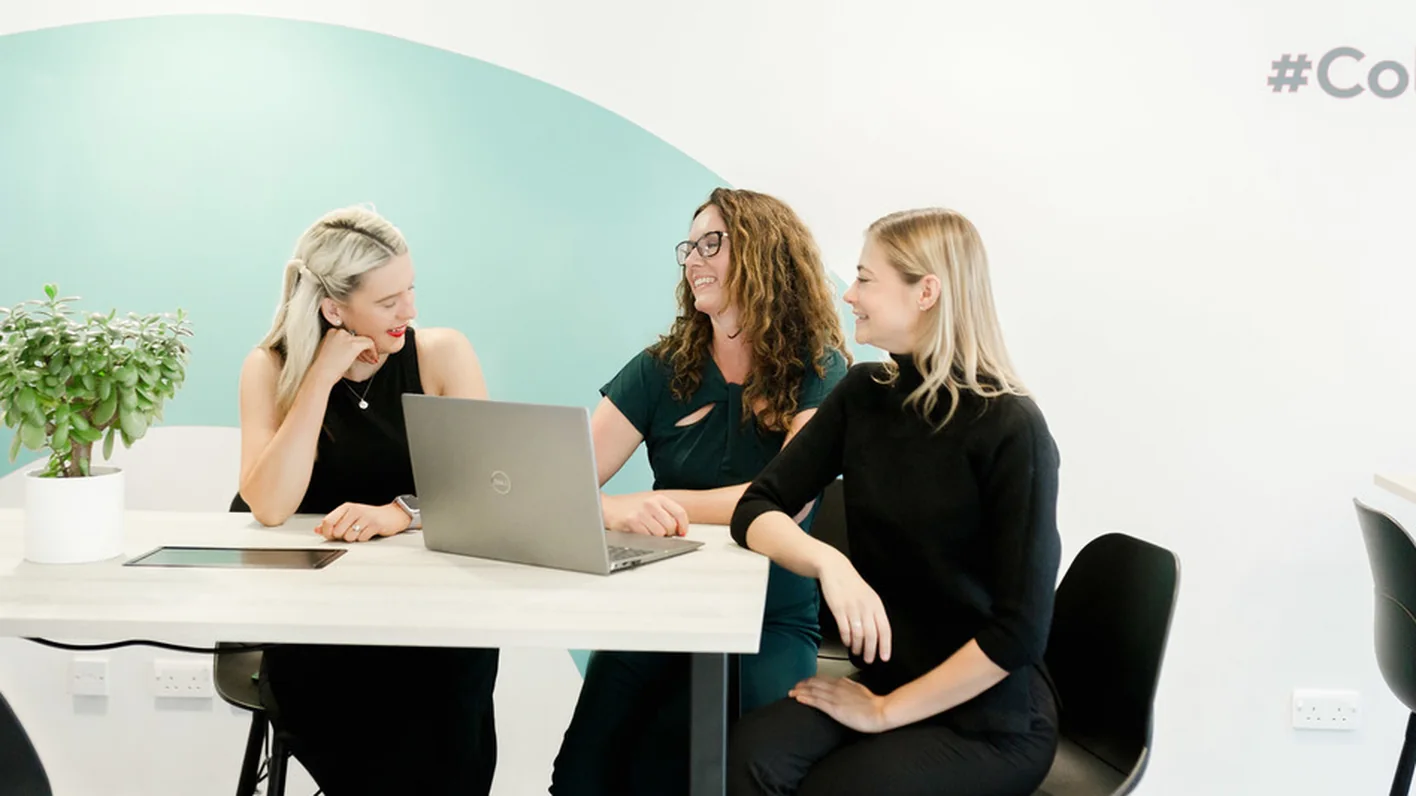 Colbea team meeting in front of the new teal brand wall graphic, part of the rebrand by CJ Creates