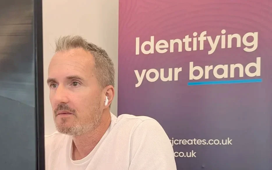 CJ Creates founder working at his desk in the Colchester studio, with the CJ Creates banner behind him