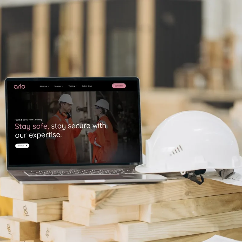 arlo health & safety and HR consultancy website home page on a laptop beside a hard hat on a building site, with the headline 'Stay safe, stay secure with our expertise', designed by CJ Creates