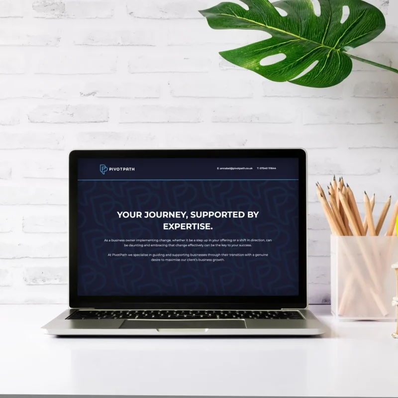PivotPath business consultancy website home page on a laptop on a desk against a white brick wall, with the headline 'Your journey, supported by expertise', designed by CJ Creates